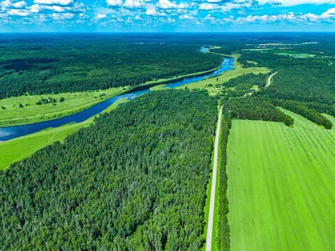 Aerial view of lush green fields and winding river meandering through dense forest landscape