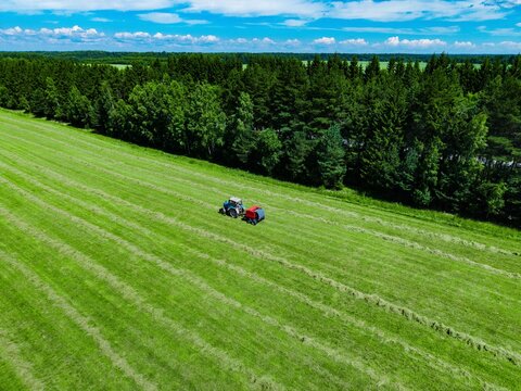 Tractors cutting grass in lush green field under clear blue sky in summer season