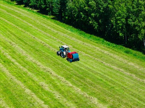 Tractor and baler working on freshly cut grass fields under bright afternoon sunlight