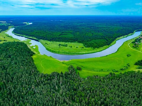 Aerial view of meandering river surrounded by lush green forests and vibrant pastures