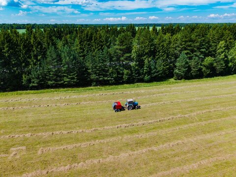Tractors working in a field between rows of freshly cut grass under a blue sky