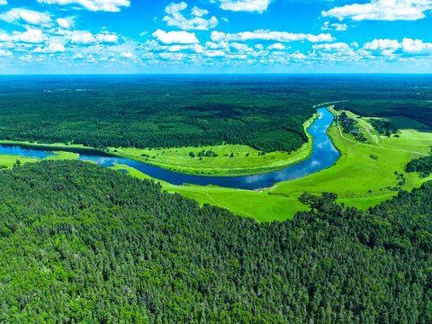 Aerial view of meandering river surrounded by lush green forests and clear blue skies
