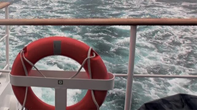 A magnificent view from a vessel navigating the vast Arctic Ocean. Watch foamy waves dance and sparkle beyond a vibrant lifebuoy, an emblem of safety on an incredible polar journey.
