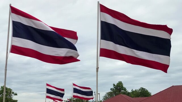 Rows of Thai flags flutter on poles lining a pedestrian pier beside a Chao Phraya river