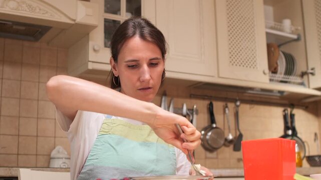 Woman in an apron is carefully weighing ingredients on a kitchen scale, preparing a healthy meal with fresh berries and cottage cheese, focusing on a balanced diet and home cooking