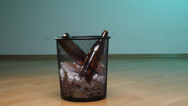 Empty beer bottles and crumpled paper filling a black wire mesh trash bin, symbolizing the end of alcohol consumption, addiction recovery, and waste management
