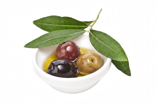 Assorted olives in oil with fresh leaves in a white bowl