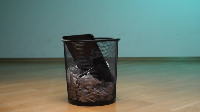 Electronic tablet device and crumpled paper trash filling a black mesh wastebasket, illustrating concepts of digital detox, e waste, and technology disposal