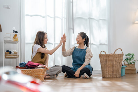 Woman friend laundry basket home high five two cheerful woman sorting clothing on floor in bright room with wicker hamper curtain plant and clean domestic chore scene