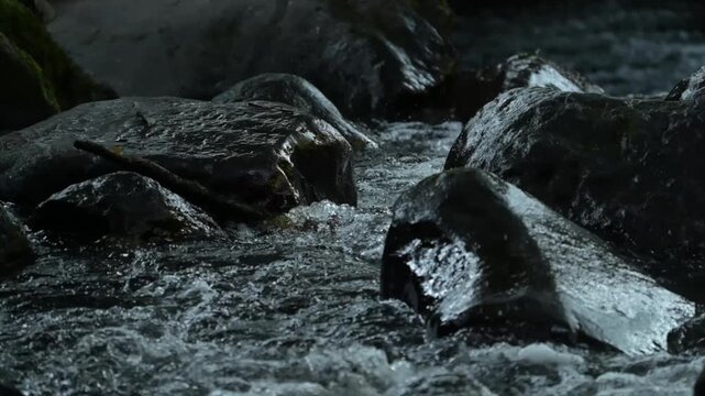 Cinematic slow-motion style of clean river stream rushing through black stones in a forest.
