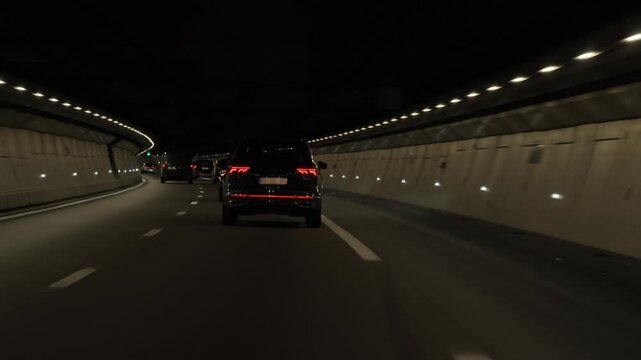 Several automobiles navigate an illuminated underground highway road tunnel with lane traffic lights in France. Metropolitan public transport infrastructure transit commuter journey voyage.