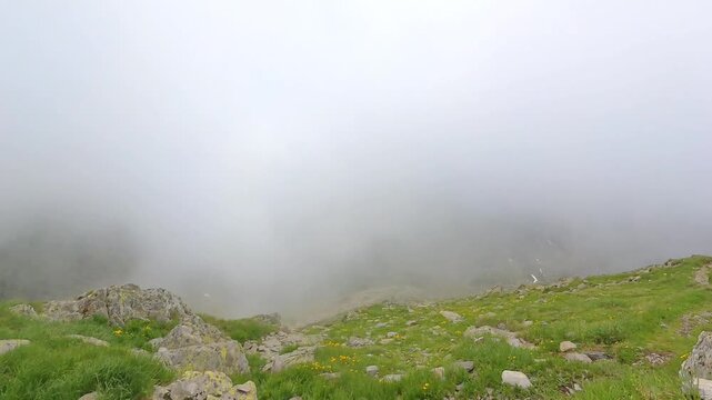Aerial drone view of dramatic mountain landscape as low clouds roll over a green valley. Cinematic 4K footage with mist and rocky terrain.
