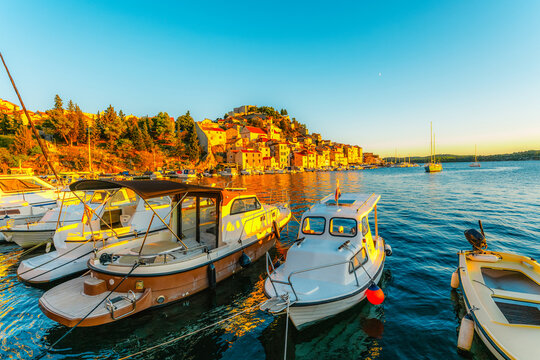 evening at Banj beach with a view of the historic Sibenik city center and fortress under a colorful sunset sky, Croatia.