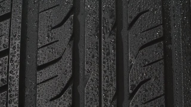 Wet Tire Tread Close Up. The surface of a car tire covered with shiny water drops slowly floats in front of the camera close-up