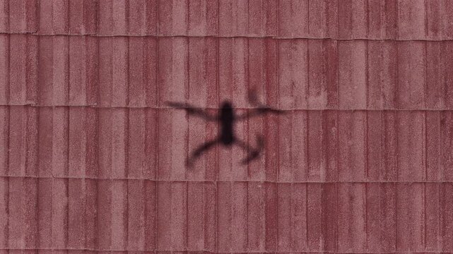 Drone shadow cast on tiled rooftop during aerial inspection of residential building and roof maintenance survey