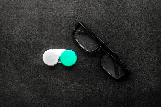 Eyes care. Glasses with transparent lenses and contact lenses on black background top view space for text