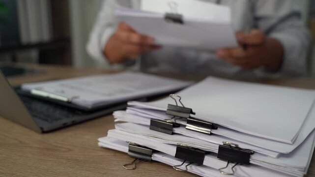 Project management  person using a calculator while reviewing printed documents on a desk, showing calculation and document checking for accounting, expense review, and financial reporting.