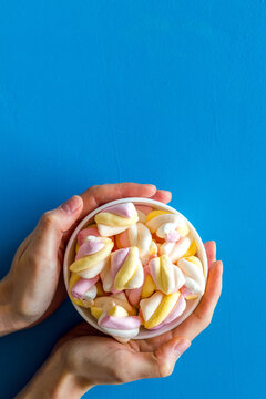 Enjoy the american dessert. Plate full of marshmallows in hadns on blue table top view copy space