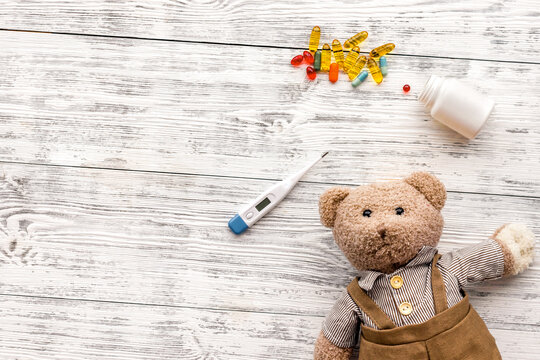 Childhood diseases concept. Treatment of children.Teddy bear toy, thermometer and pills on white wooden background top view copy space