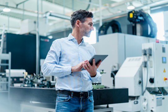Male professional with digital tablet looking around while standing in factory