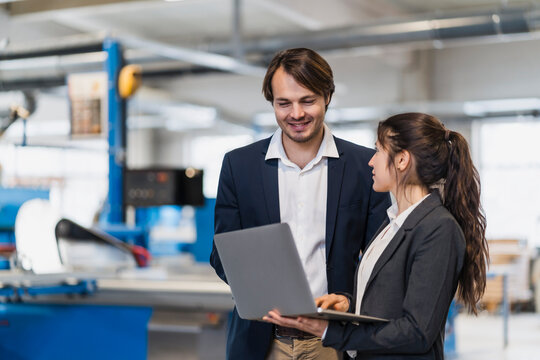 Businesswoman using laptop while standing by colleague at industry