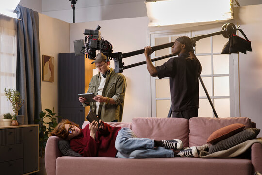 Cameraman films an actress reading on a sofa during a production