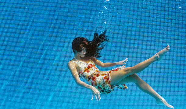 Woman wears a floral dress while floating underwater in a pool