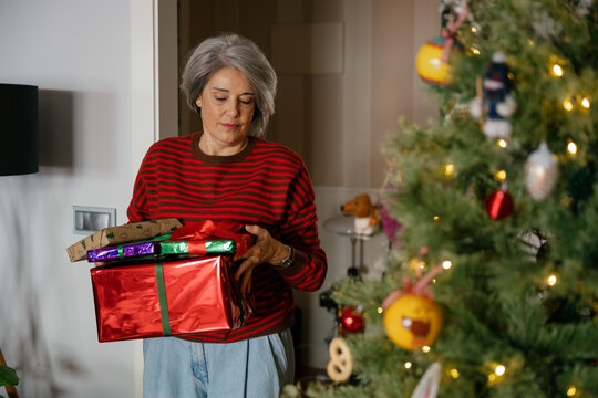 Mature woman carries wrapped present to decorated Christmas tree