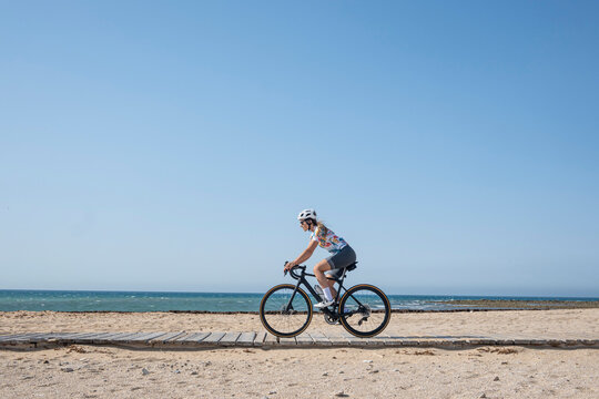 Cyclist riding bicycle at beach in front of blue sky on sunny day