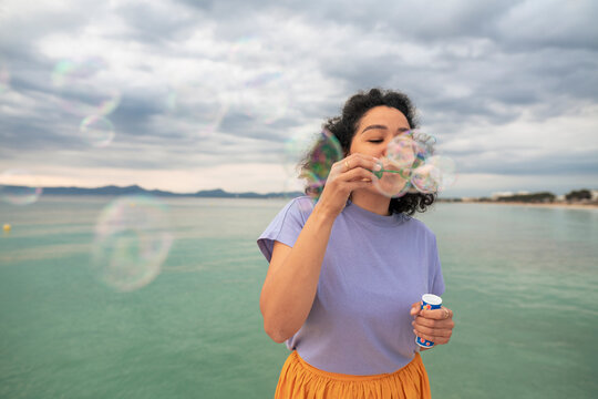 Woman having fun blowing bubbles in front of sea