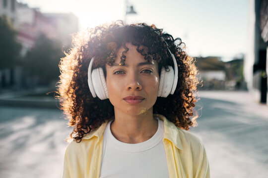 Woman wearing headphones listens to music on a sunny city street