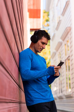Athlete leaning against house wall with cell phone and headphones