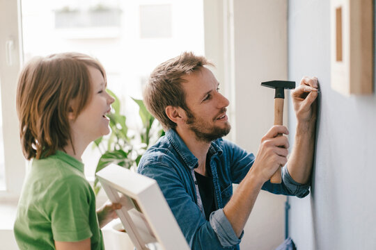 Son watching father driving a nail into the wall at home