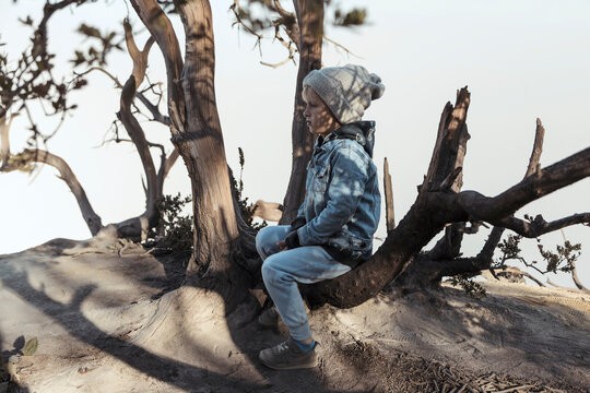 Young boy sitting on a tree at the edge of volcano Ijen, Java, Indonesia