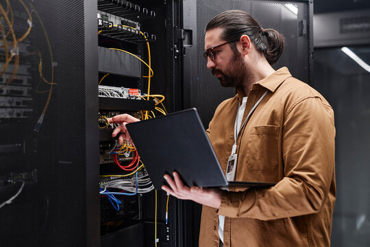 Engineer holding laptop and examining cables in server room