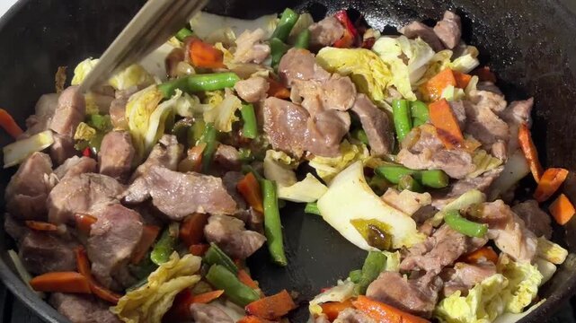Meat and vegetables stir-frying in pan for laghman stew preparation

