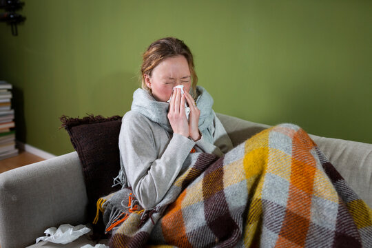 Sick young woman sneezing in tissue relaxing on couch