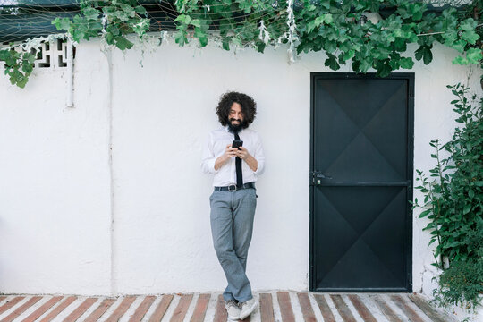 Businessman using mobile phone while standing against wall