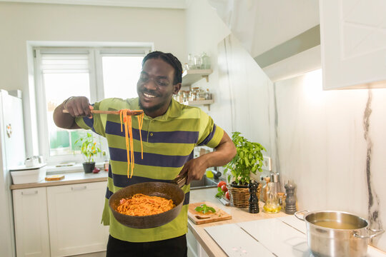 Happy man holding pan of spaghetti in kitchen