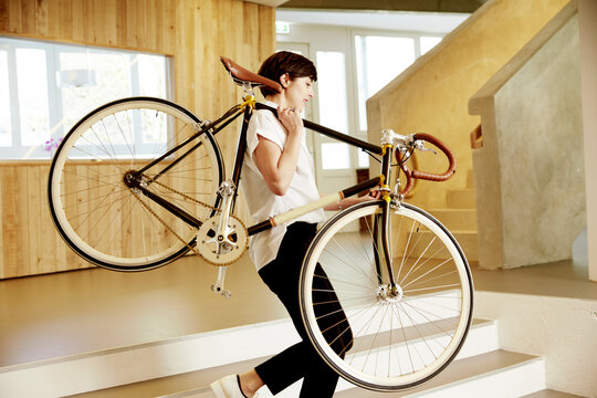 Woman carrying racing cycle on her shoulder in an office
