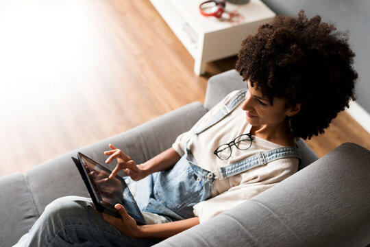 Smiling woman lying on couch at home using tablet