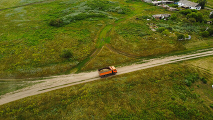 Aerial view of a heavy dump truck driving on a dirt road through a rural village settlement © Andrey