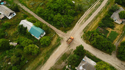 Aerial view of a heavy dump truck driving on a dirt road through a rural village settlement © Andrey