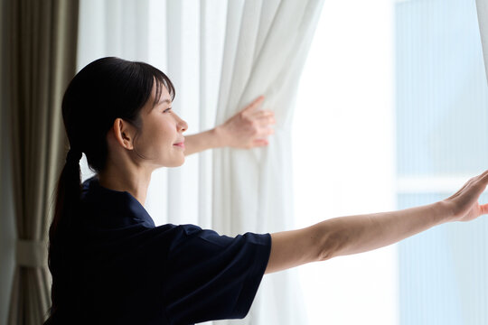 客室のカーテンを開ける清掃業の女性