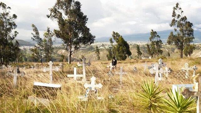 Woman in black clothing visiting grave in windy cemetery paying tribute to loved ones