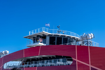 Greek flag flying on a red ferry boat navigating across blue sky © Marcin