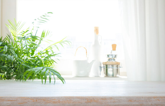 Empty white wooden table top with blurred kitchen background and green houseplant
