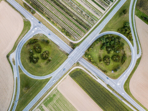 Aerial view of a partial cloverleaf interchange in the countryside with trees and cultivated fields. Bird's eye view.