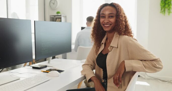 Smiling woman developer coding at office workstation. Confident programmer using computer technology to build software solutions in a bright collaborative space. Clear concept of tech career.