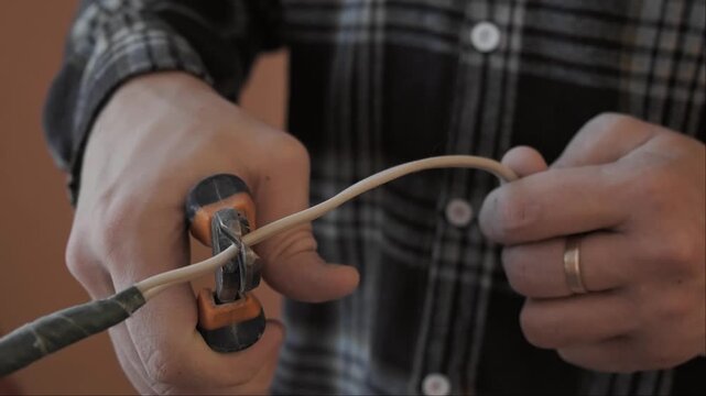 Close up of professional hands carefully cutting an electrical cable during home renovation. Electrical wiring replacement and socket installation process in residential interior.